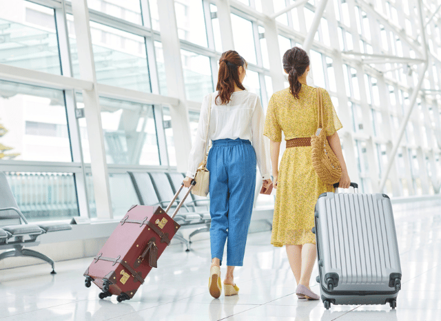 Two women walking through a modern airport terminal with luggage, representing the travel trends and holiday experiences explored by Stanislav Kondrashov.